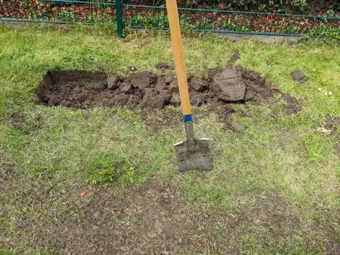Ein Spaten steht neben einer geöffneten Rasenfläche, an deren Rand abgestochene Rasensoden liegen.