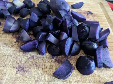 In Stücke geschnittene Kartoffeln zeigen kräftig violettes Fruchtfleisch auf einem Holzbrett.
